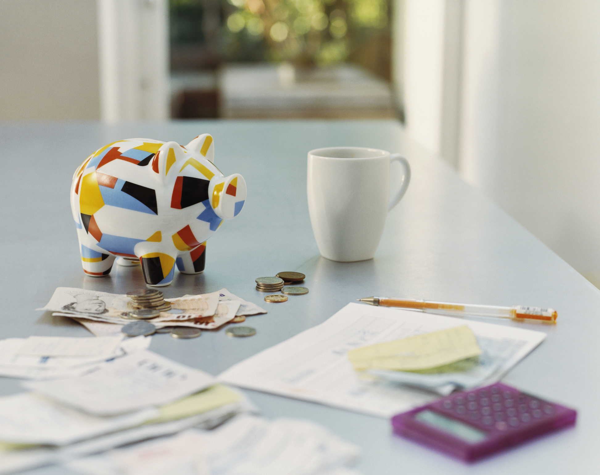 Piggybank, British Currency, Calculator, Receipts And A Mug On A Table